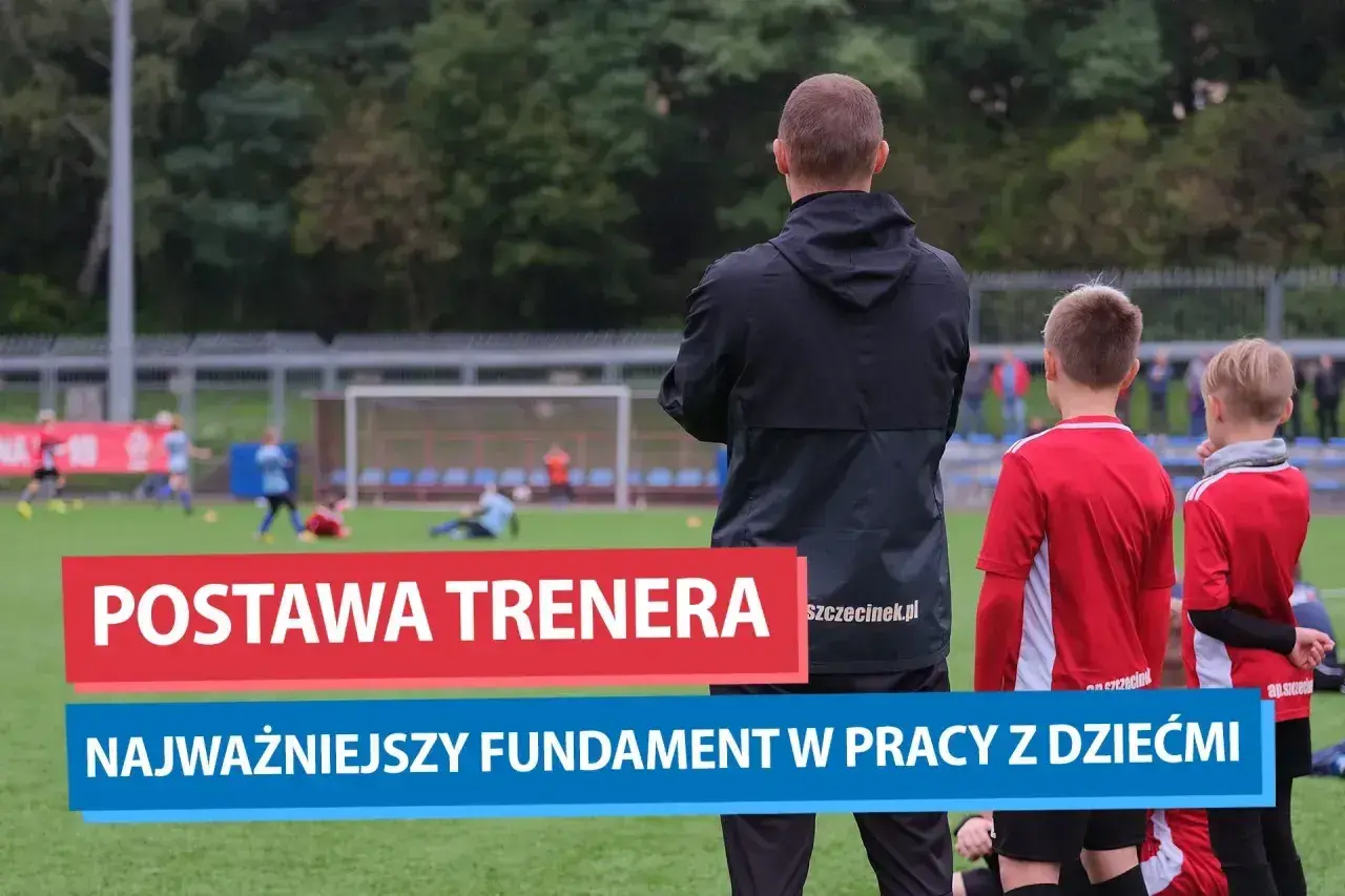 Trener motywacyjny obserwuje młodych piłkarzy na boisku. Jego postawa to fundament pracy z dziećmi.