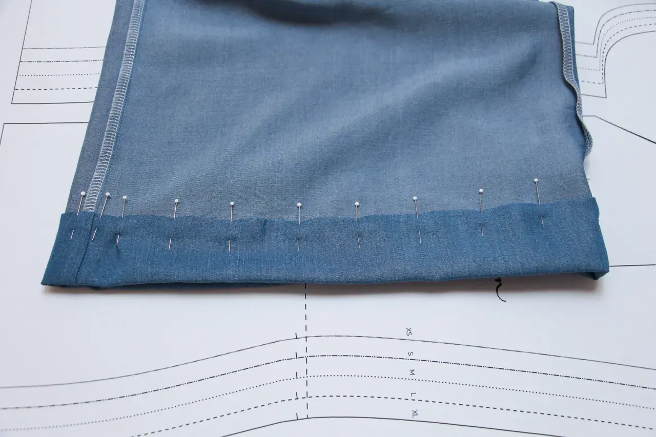 Pins secure the folded hem of blue knit pants, ready for sewing. This image shows a step in how to hem knit pants.