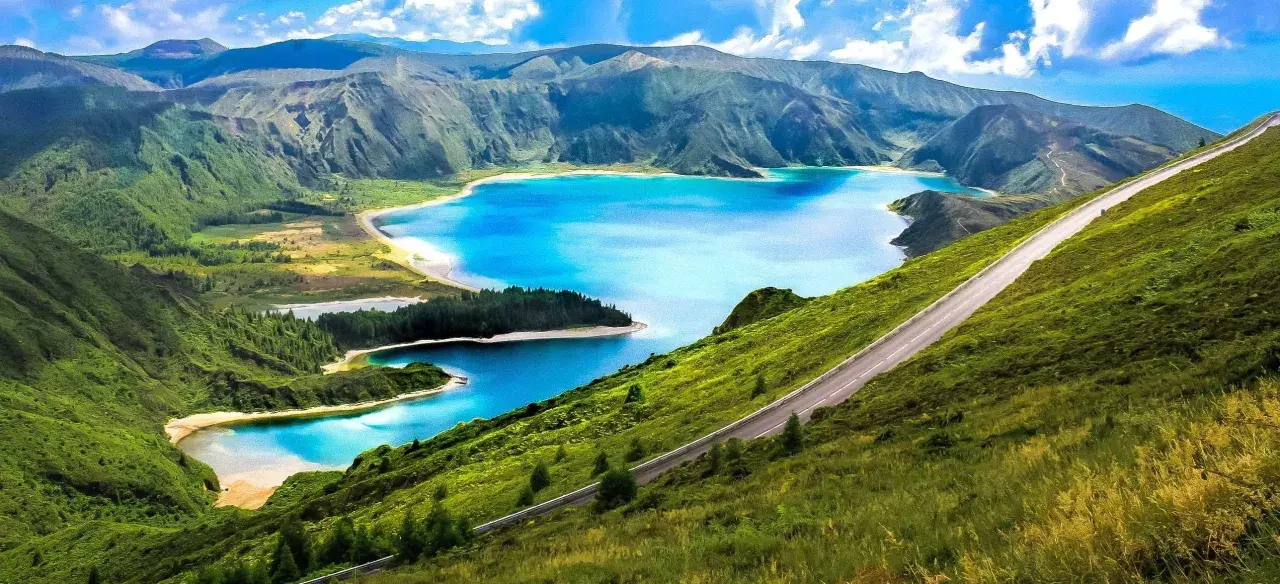Carretera serpenteante en una ladera verde con lagos azules y montañas al fondo, un paisaje idílico de Portugal en octubre.