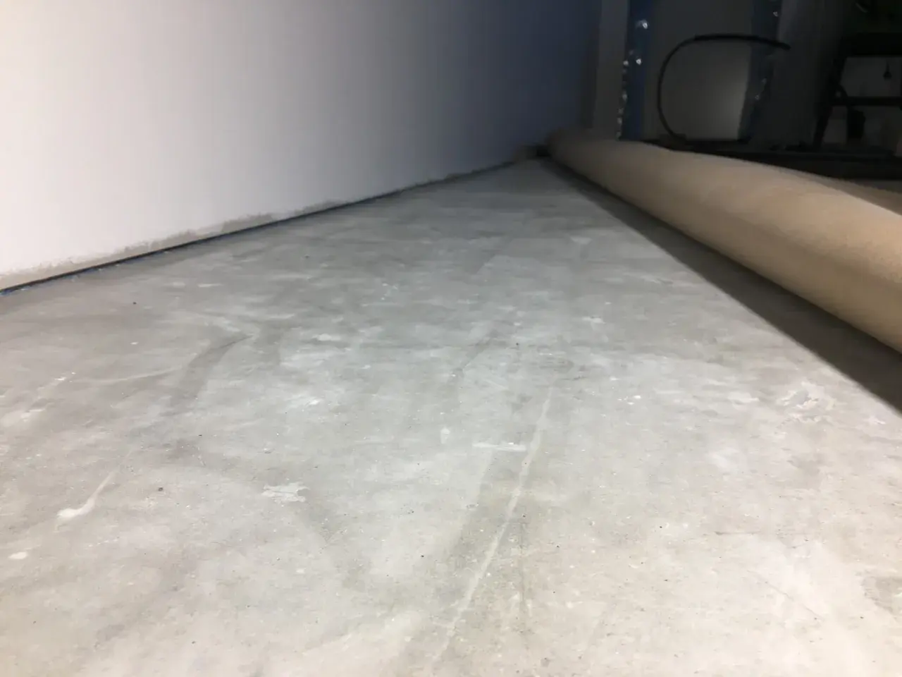 Ojämn betongyta som väntar på att slipa betong för en jämn finish. En rulle skyddspapper ligger längs väggen.