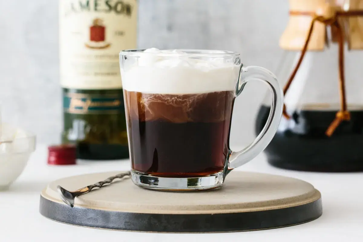 Pyszny drink z kawą, z bitą śmietaną i butelką Jameson w tle. Idealny na chłodne wieczory.