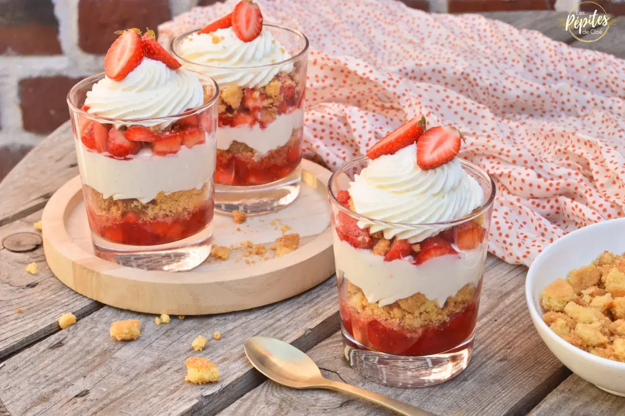 Trois verrines fraise mascarpone facile, garnies de crème fouettée et de fraises fraîches, sur une table en bois.