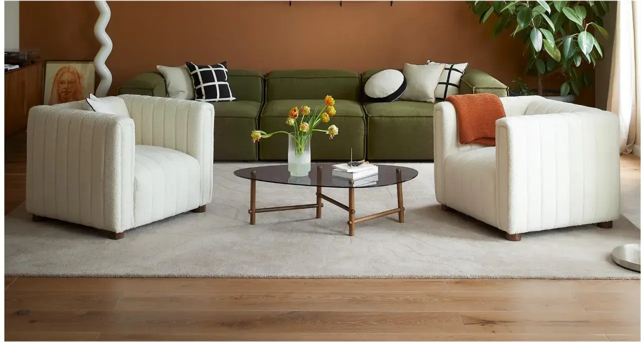 Ein grünes Sofa mit Kissen, die das Sofa dekorieren und richtig kombinieren. Zwei weiße Sessel und ein Couchtisch mit Blumen.