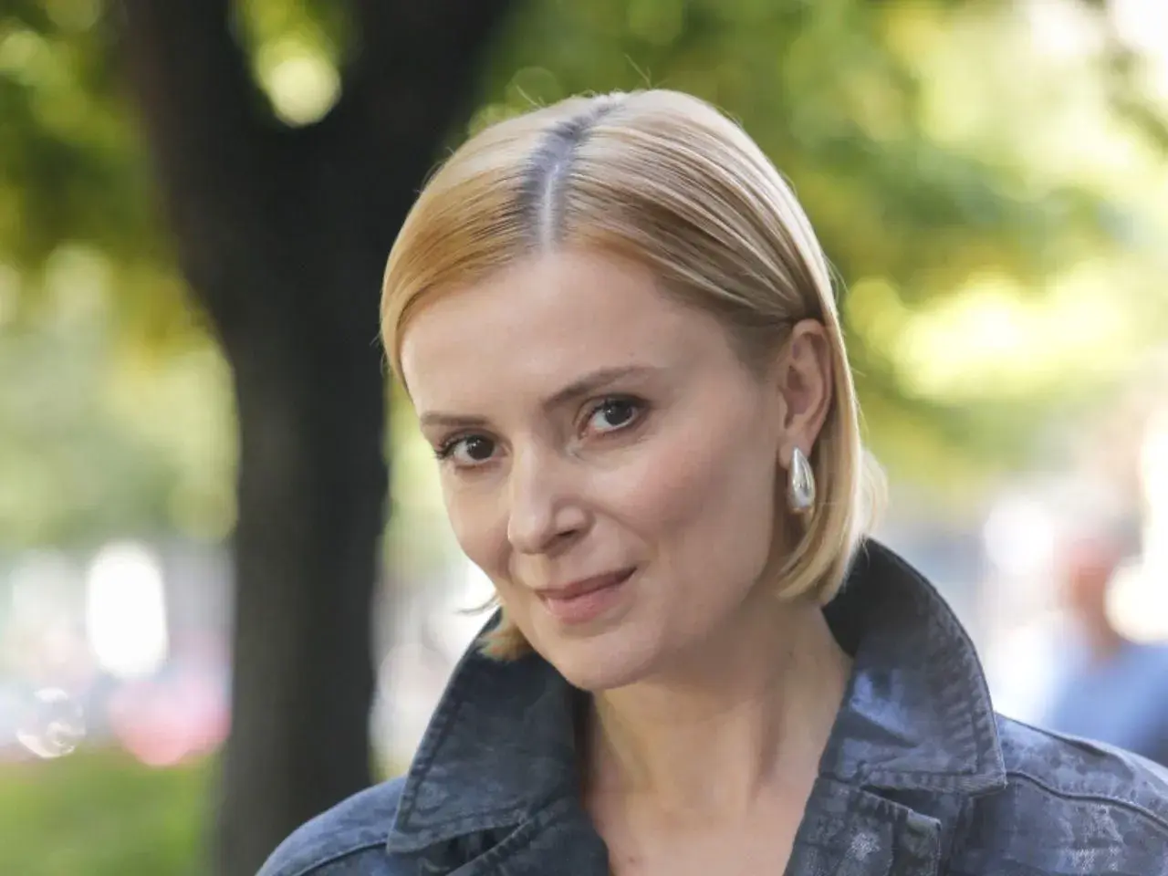 Portret Haliny Młynkowej z krótkimi blond włosami, w kurtce, na tle drzew.