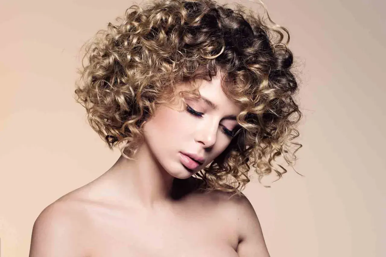 Mujer con un moderno bob cortes de pelo rizado, con reflejos rubios y castaños, mirada serena.