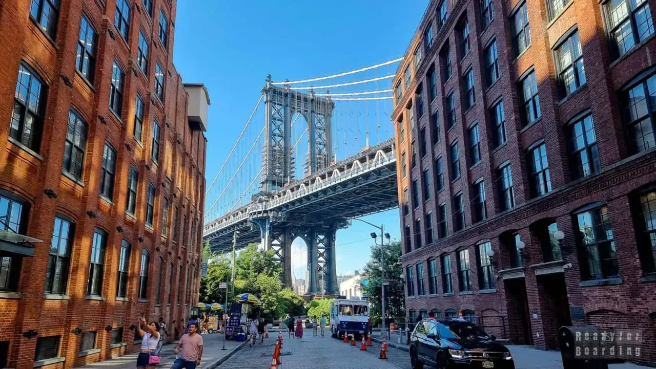 Ulica w **brooklyn** z ceglanymi kamienicami i majestatycznym mostem w tle.
