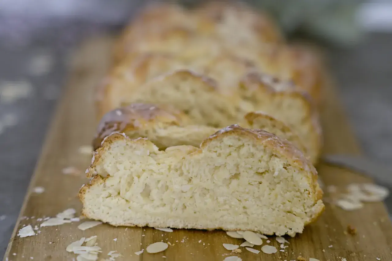 Ein frisch gebackener Hefezopf, aufgeschnitten auf einem Holzbrett, mit Mandelblättchen bestreut. Ein leckeres Rezept für den Sonntagsbrunch.