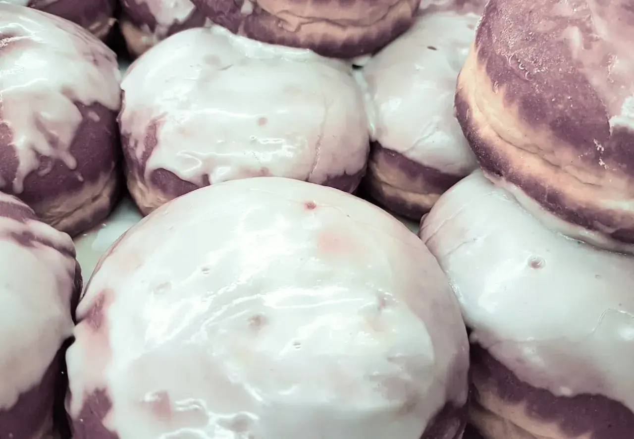 Pączki z fioletowym nadzieniem, polane błyszczącym lukrem z cukru pudru, kuszą swoim wyglądem.