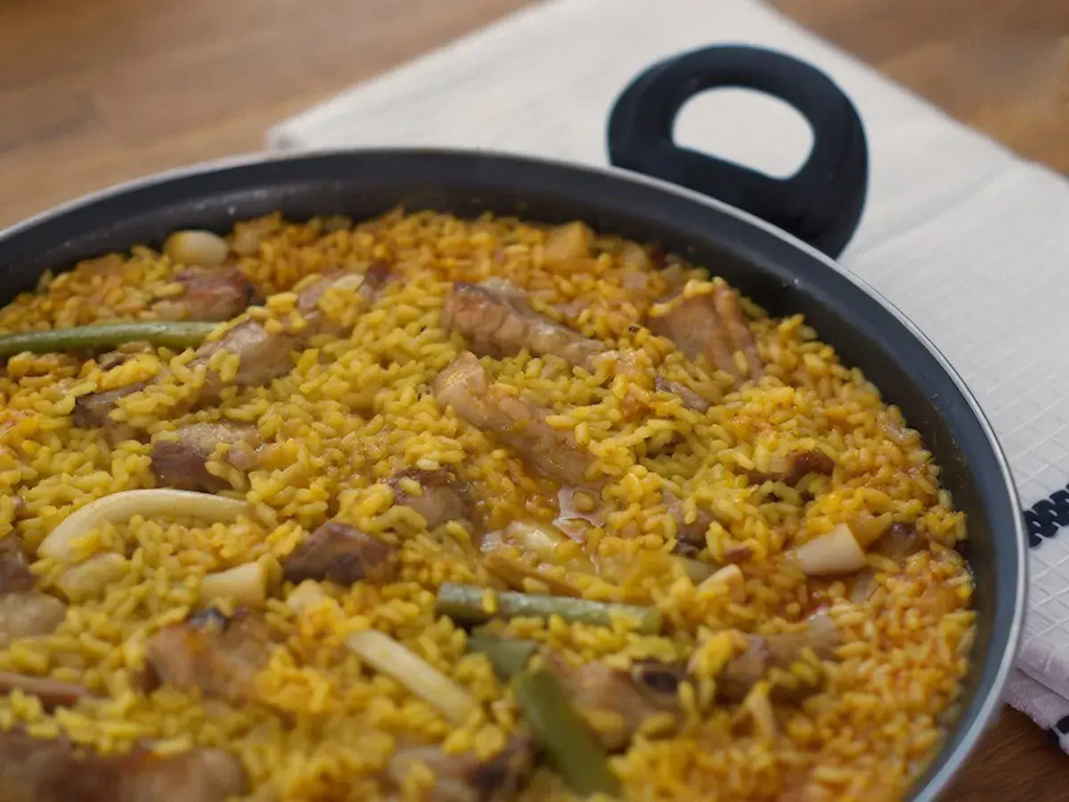 Un delicioso arroz meloso con trozos de carne, judías verdes y calamar en una paellera.