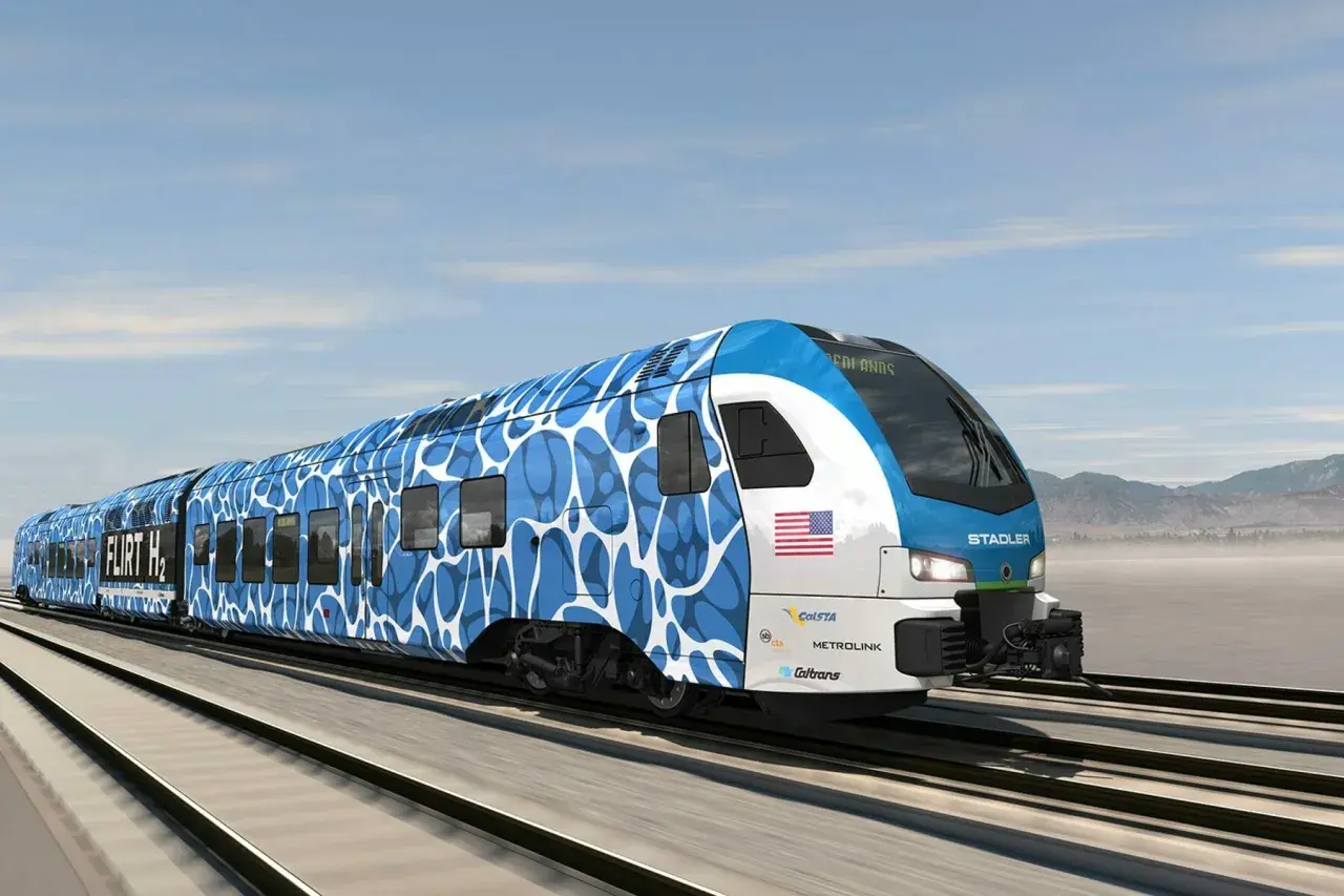 Nowoczesny pociąg Stadler FLIRT H2 z niebiesko-białym wzorem pędzi po torach.