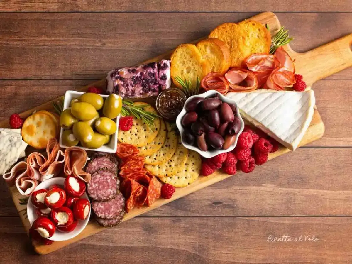 Un invitante tagliere salumi e formaggi con olive, lamponi, pane tostato e vari salumi.