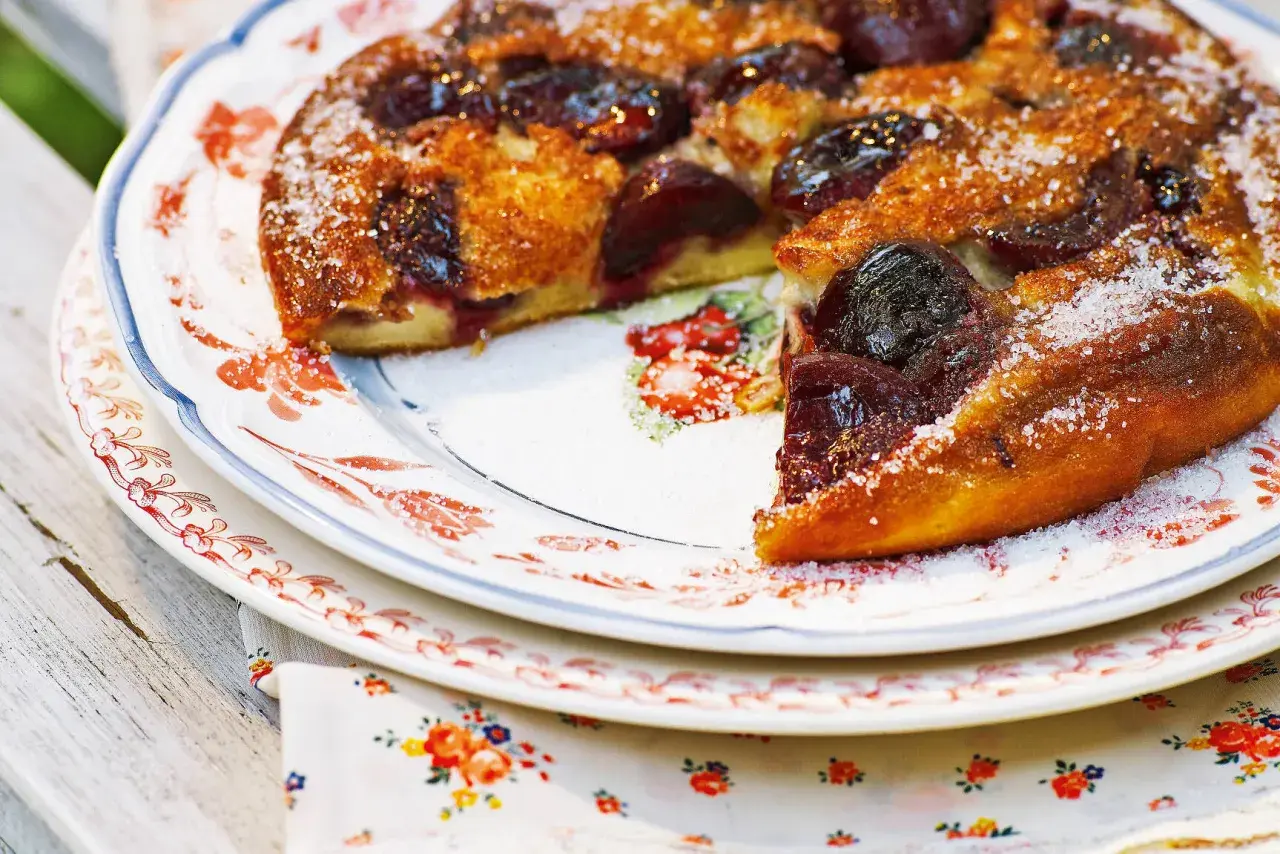 Ein goldbrauner Pfannkuchen mit Kirschen, bestreut mit Zucker, auf einem Teller mit Blumenmuster.
