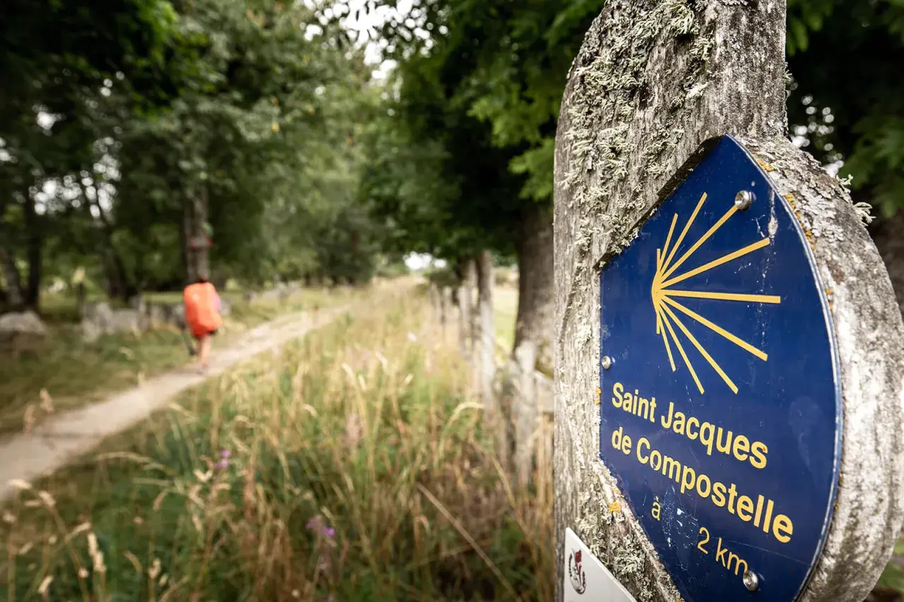 Panneau Saint Jacques de Compostelle sur le chemin, indiquant la direction de Conques. Un pèlerin s'éloigne sur le sentier.