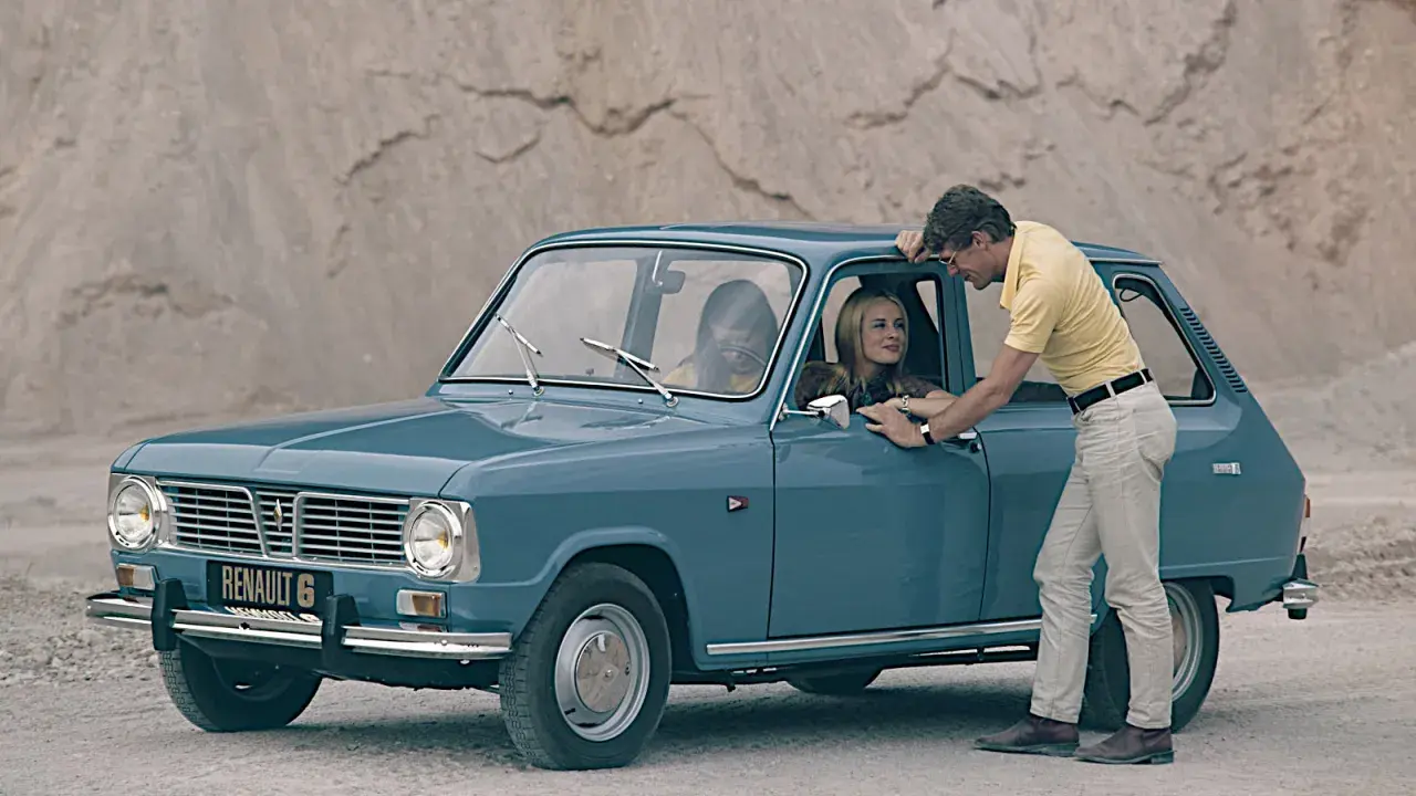 En man lutar sig mot en blå Renault 6, en av många gamla Renault-modeller, medan en kvinna sitter bakom ratten.