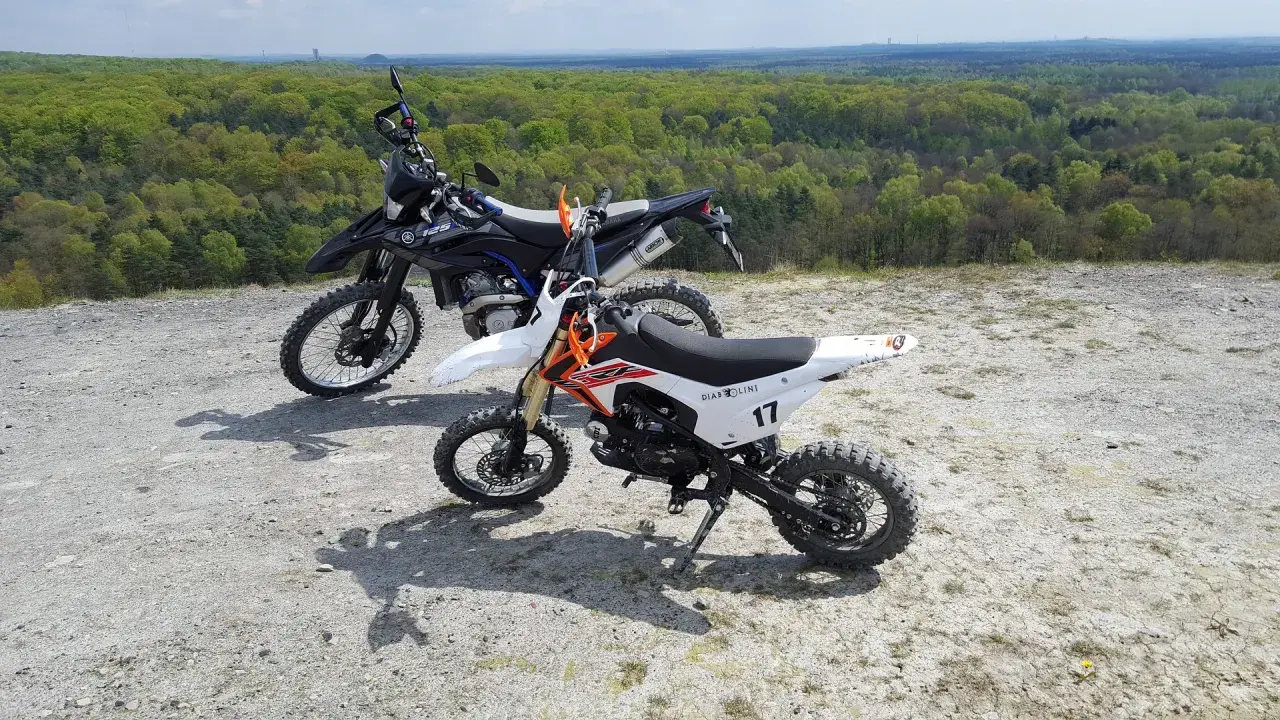 Dwa motocykle crossowe na tle lasu. Czy crossem można jeździć po ulicy? Te maszyny są stworzone do terenu.