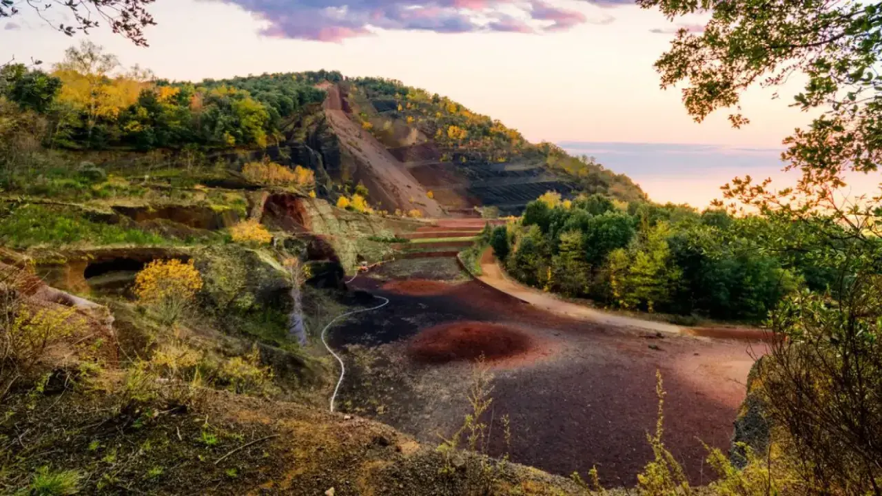 Paisaje del parc natural de la zona volcànica de la Garrotxa con laderas escalonadas, vegetación otoñal y el cielo rosado del atardecer.