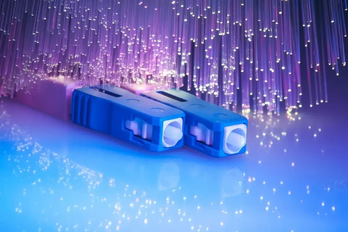 Connecteurs bleus pour télécommunication fibre optique, entourés de fils lumineux violets.