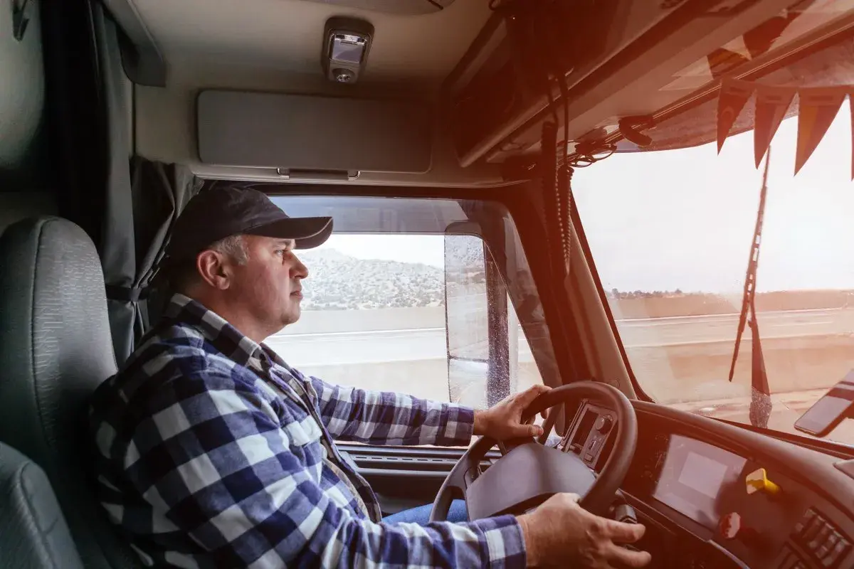 Ein LKW-Fahrer im karierten Hemd lenkt seinen Truck. Sein Gehalt ist ein wichtiger Faktor für seine Arbeit.