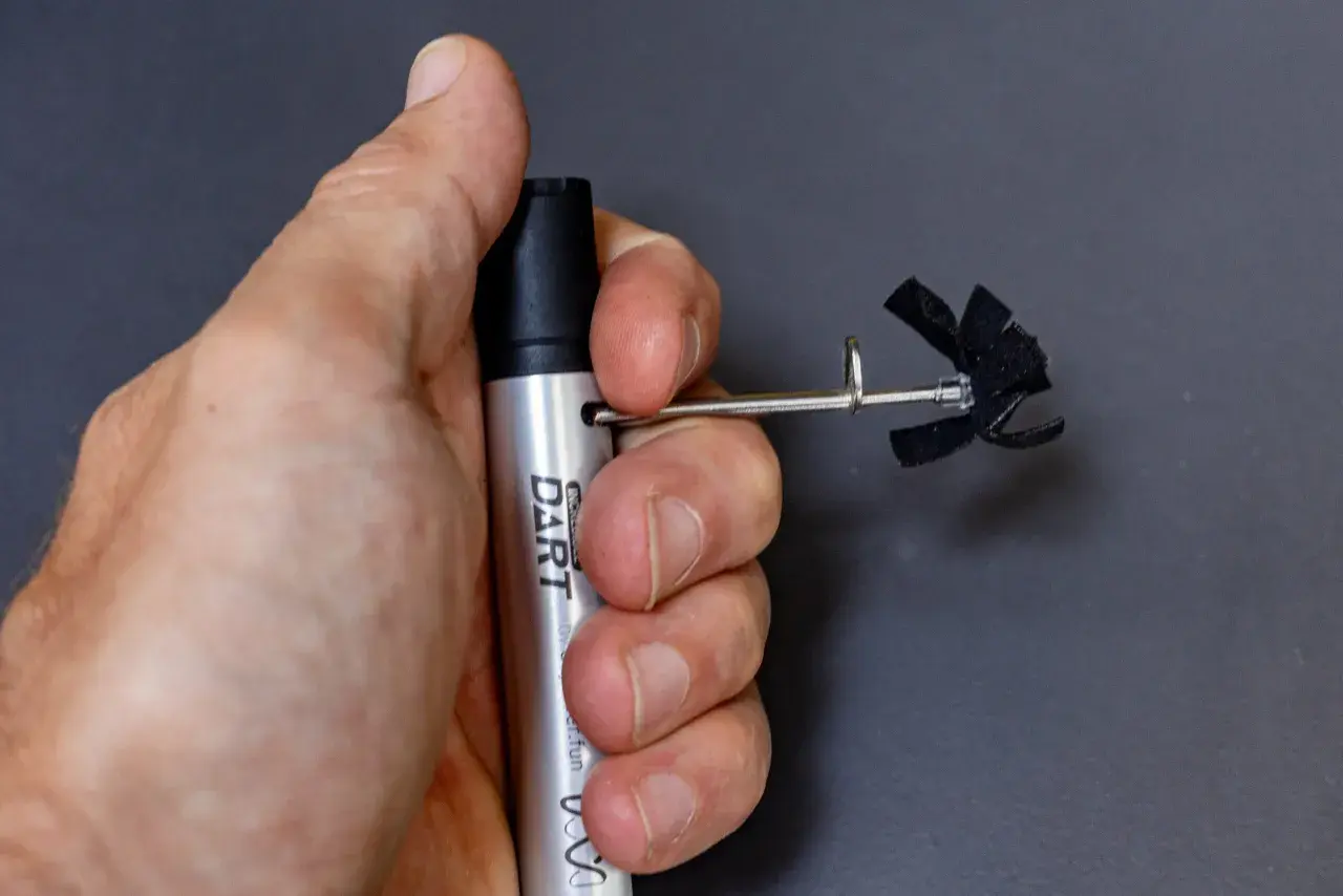 A hand holds a silver "DART" marker with a small, black, propeller-like attachment. This is part of a stans dart review.