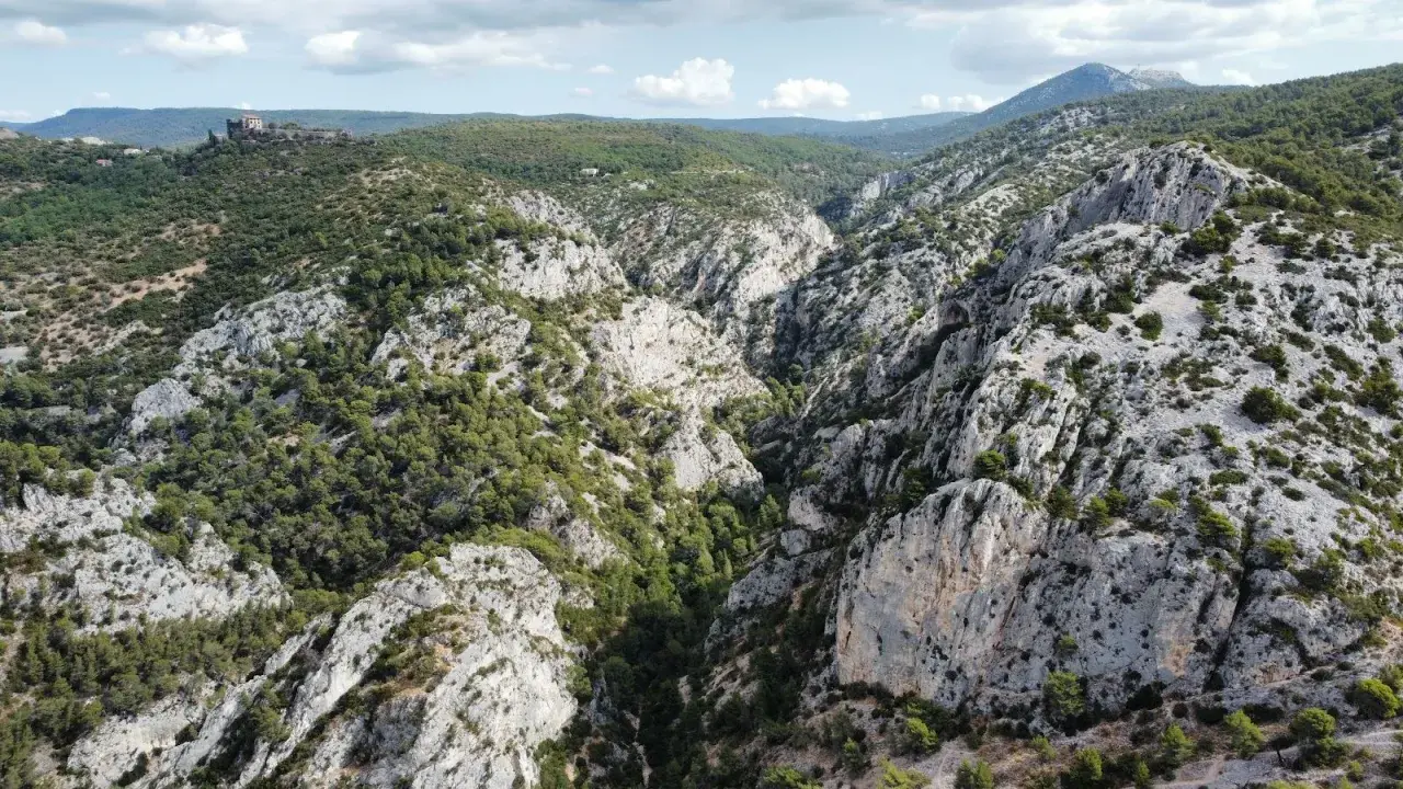 Vue aérienne de la **gorge d'Ollioules**, un canyon rocheux bordé de pins, avec un château en ruines sur une colline au loin.