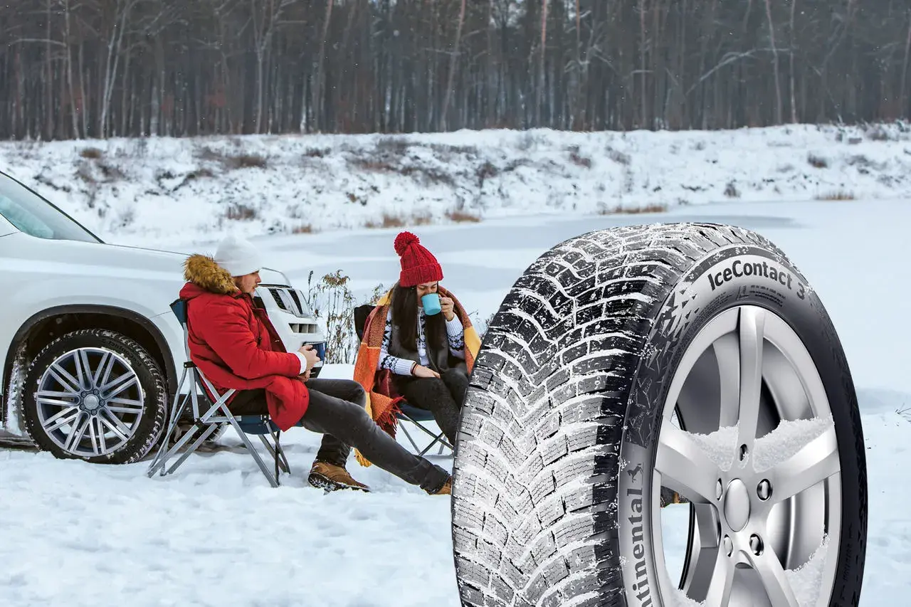 Ett par njuter av en paus i snön bredvid en bil, med en vinterdäck i förgrunden. Välj dubb eller dubbfritt för din trygghet.