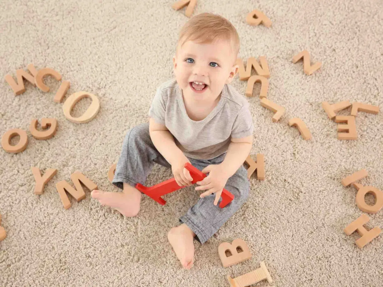 Bambino sorridente circondato da lettere di legno, un modo divertente per iniziare a capire come sviluppare il linguaggio nei bambini.