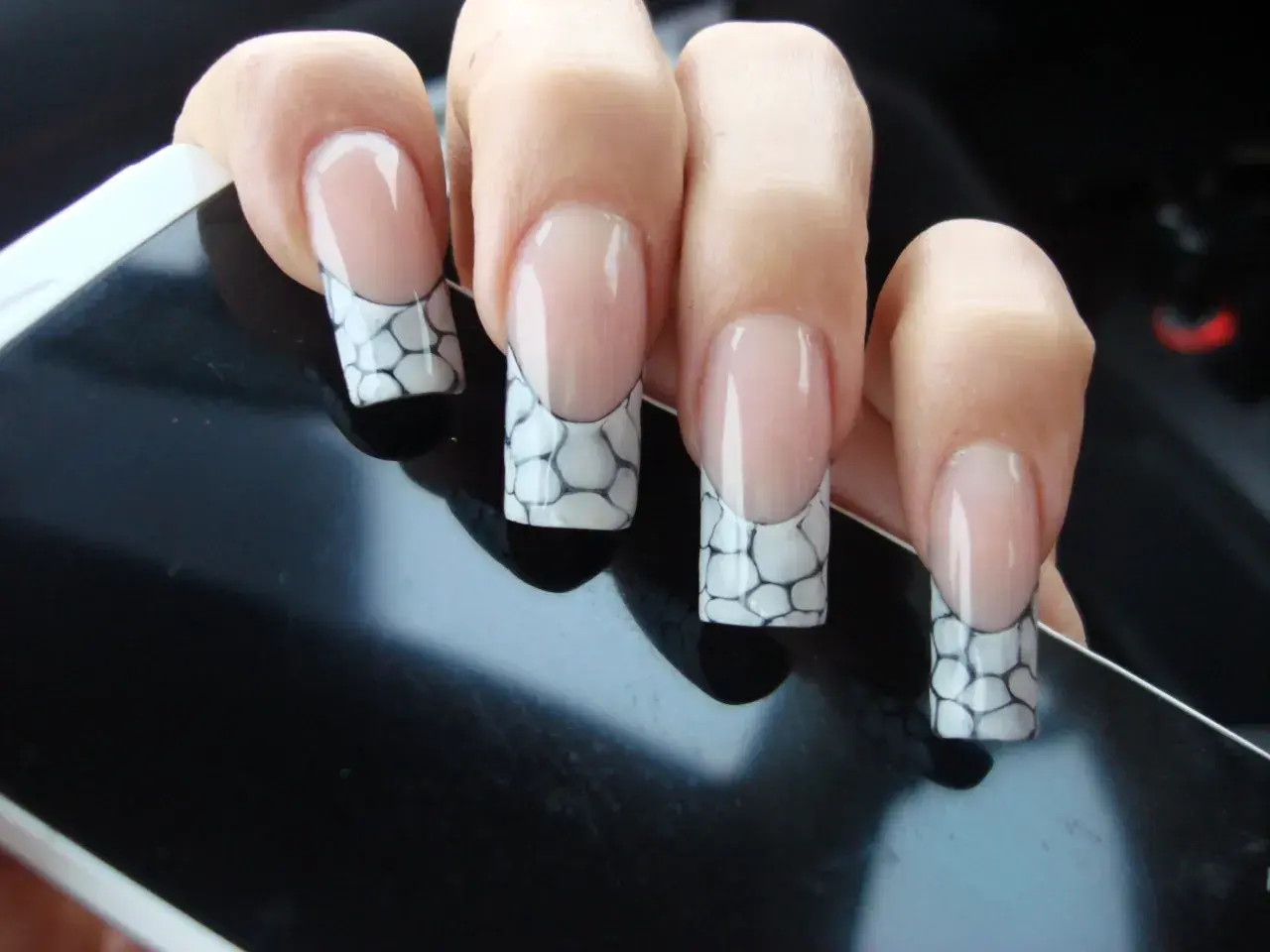 Manucure française avec un motif écaille de tortue sur les ongles, posée sur un écran noir.