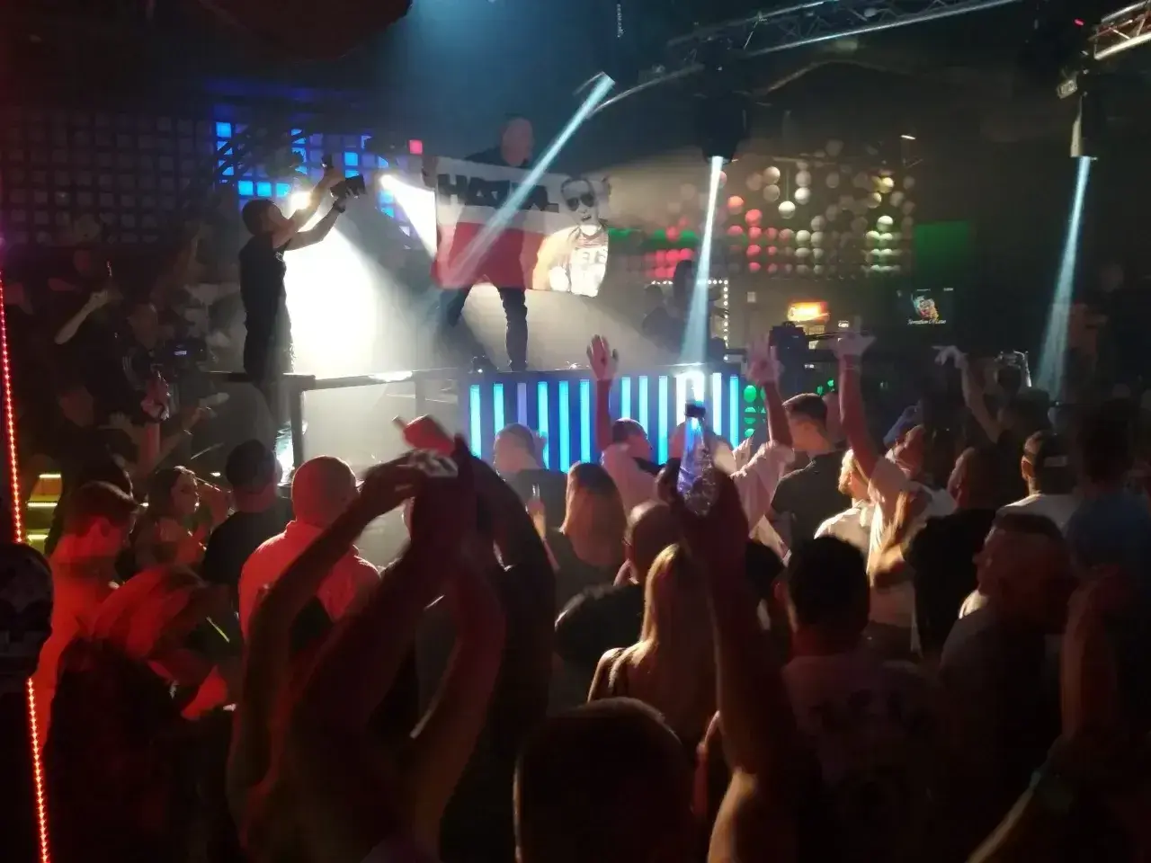 Tłum na parkiecie klubu, DJ na scenie z flagą Polski, światła i energia prawdziwego rave.