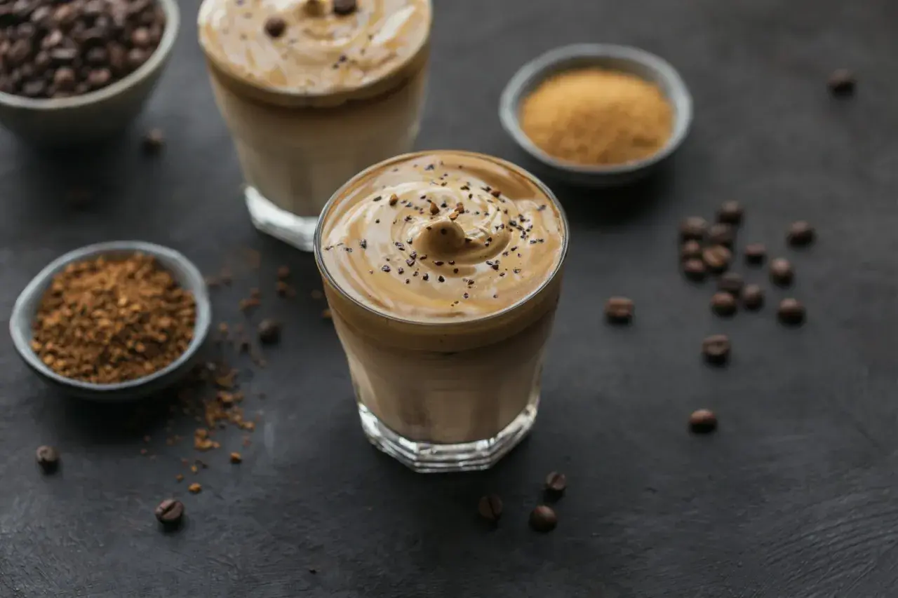 Dwa szklanki kawy mocha mousse z pianką i posypką z kawy. Obok miseczki z kawą rozpuszczalną i cukrem.