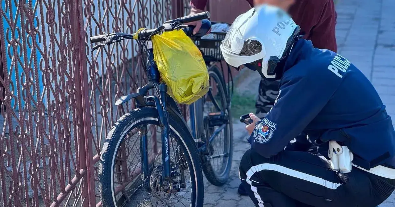Policjant sprawdza rower na drodze dla rowerów. Żółta torba wisi na kierownicy.