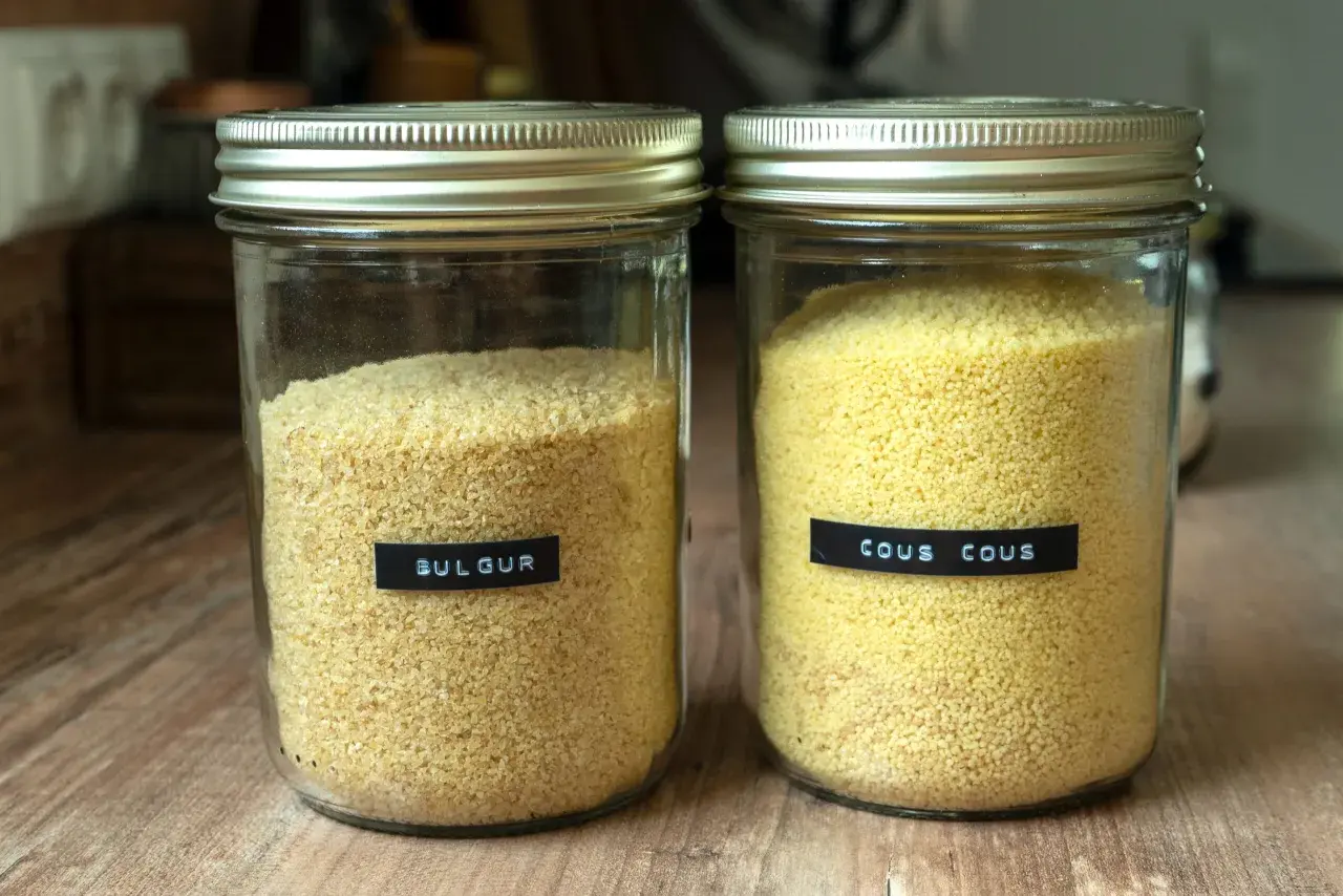 Zwei Gläser mit Getreide: links Bulgur, rechts Couscous. Beide sind gut sichtbar und bereit für die Zubereitung.