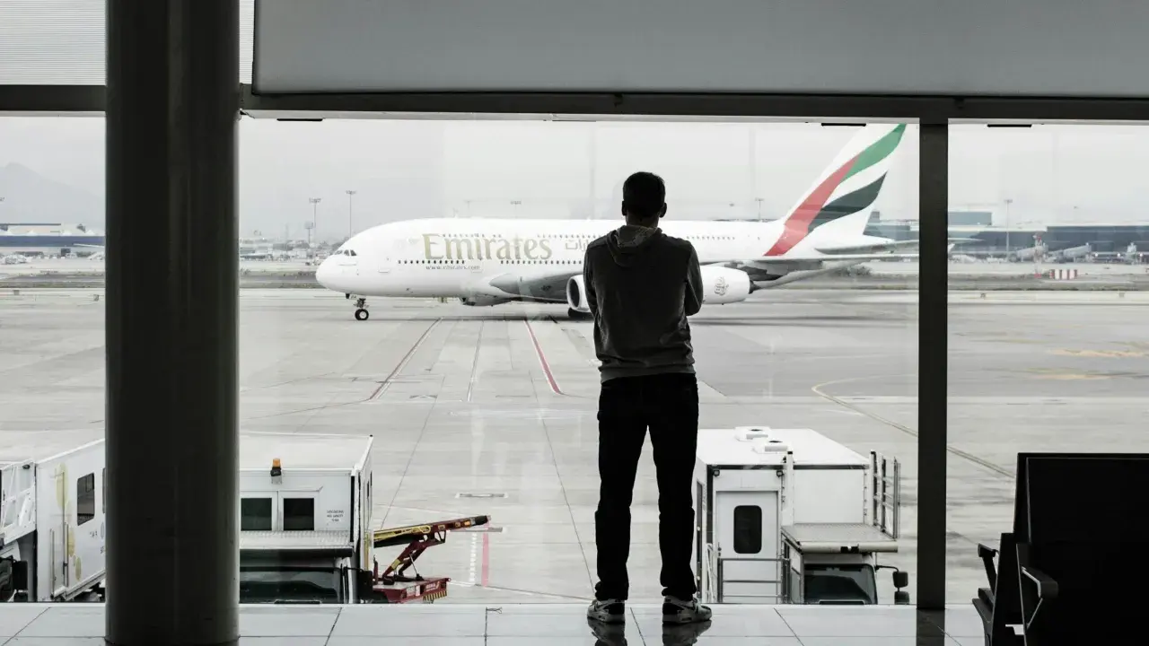 Mężczyzna w bluzie patrzy na samolot Emirates. Czeka na swój bagaż podręczny.