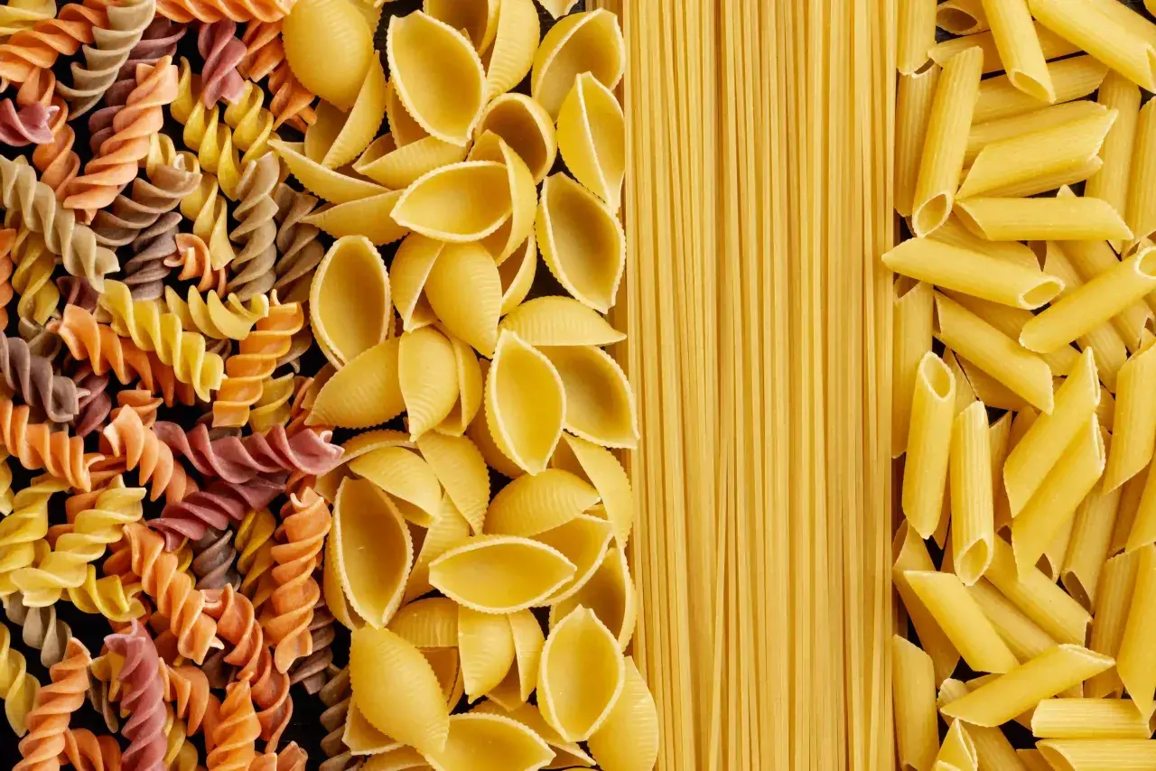 Różne rodzaje makaronu: kolorowe fusilli, muszelki, spaghetti i penne. Wybór wpływa na indeks glikemiczny posiłku.