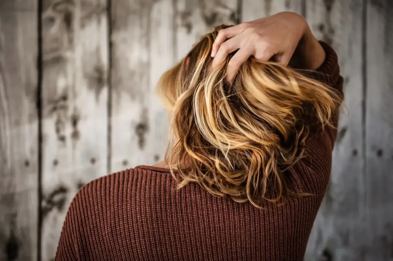 Capelli biondi mossi, una mano li accarezza. La vitamina C capelli dona lucentezza e forza.