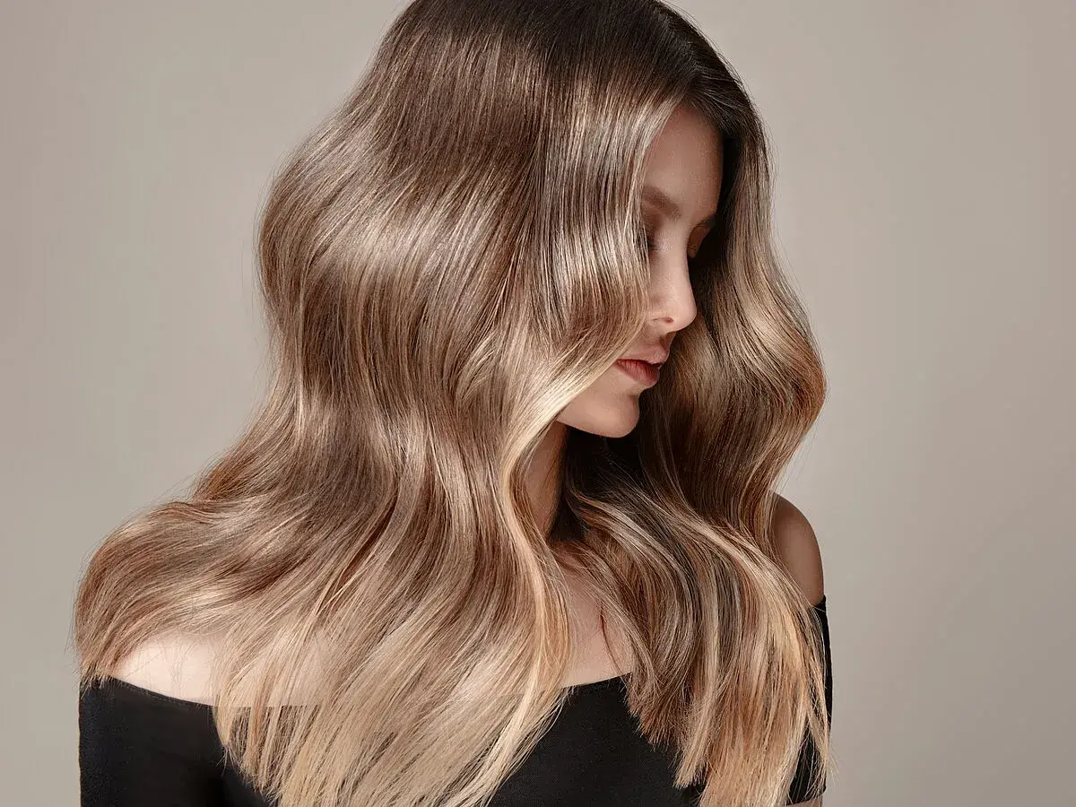 Mujer con cabello largo y ondulado en tonos castaños y rubios, ideal para quienes buscan cómo quitar el tinte del cabello y dejarlo natural.