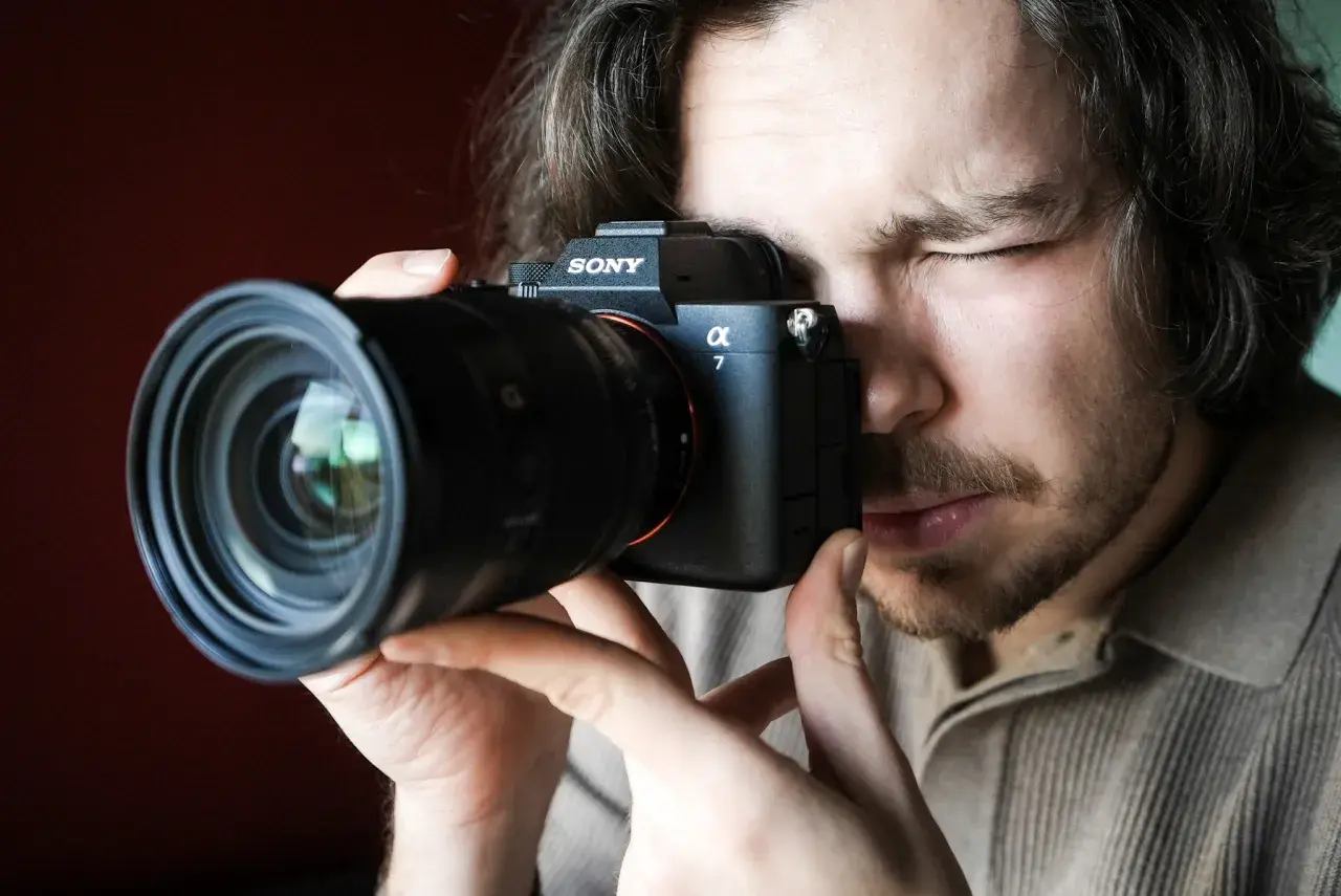 Mężczyzna zamyka oko, patrząc przez wizjer aparatu Sony Alpha 7. Premiera Sony a7 IV budzi emocje.