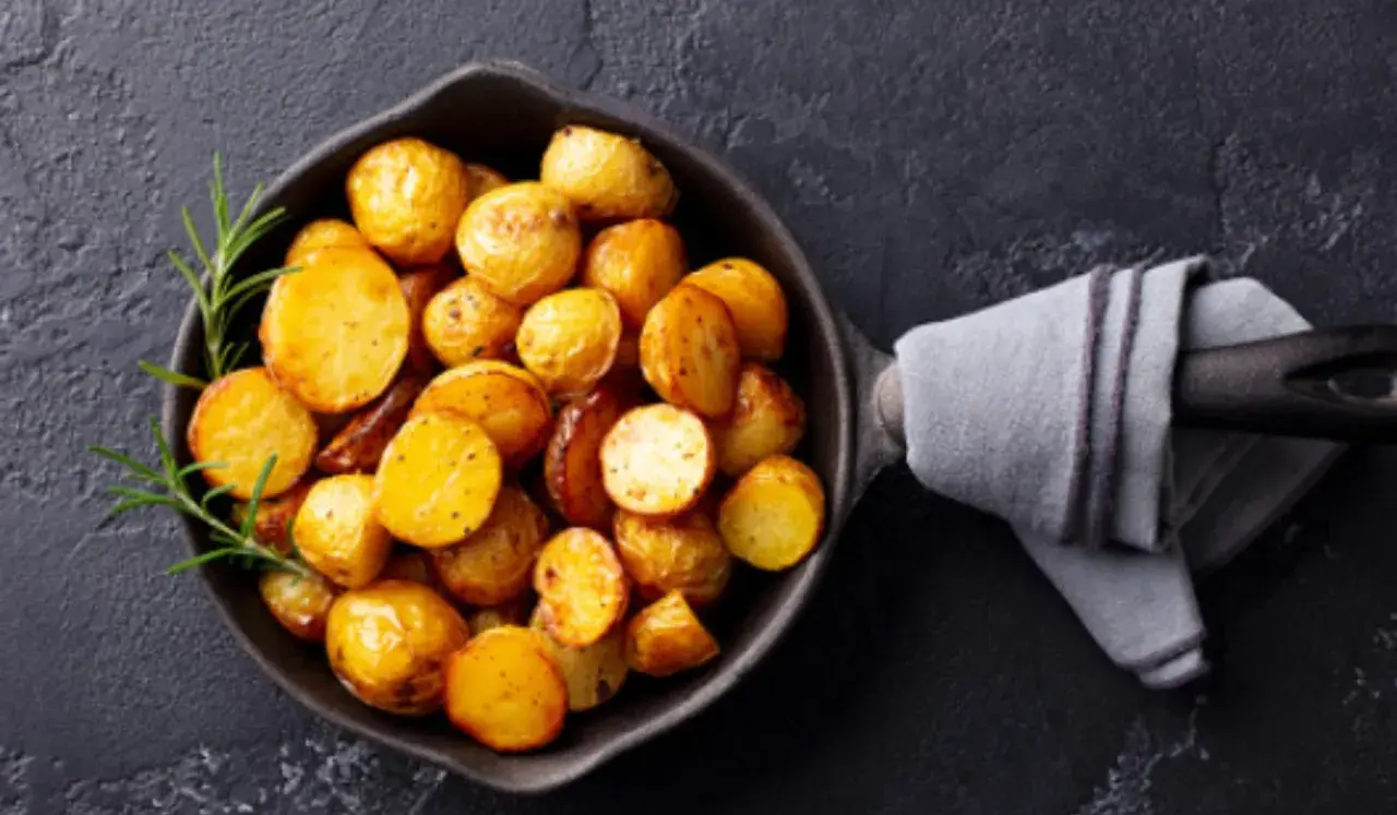 Patatas doradas y tiernas listas para cocer, con romero fresco en una sartén de hierro fundido.