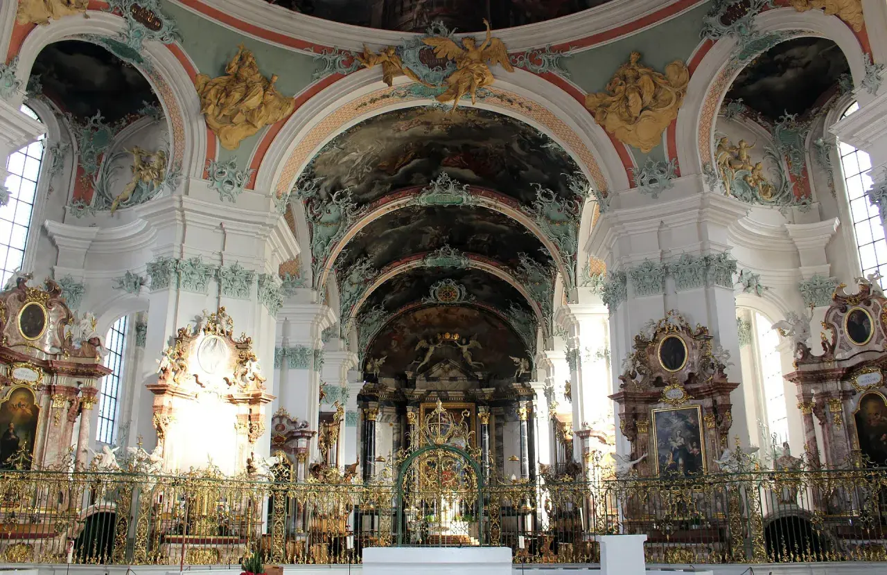 Wnętrze kościoła w stylu barokowym, z bogatymi zdobieniami, freskami na sklepieniach i złotymi elementami.