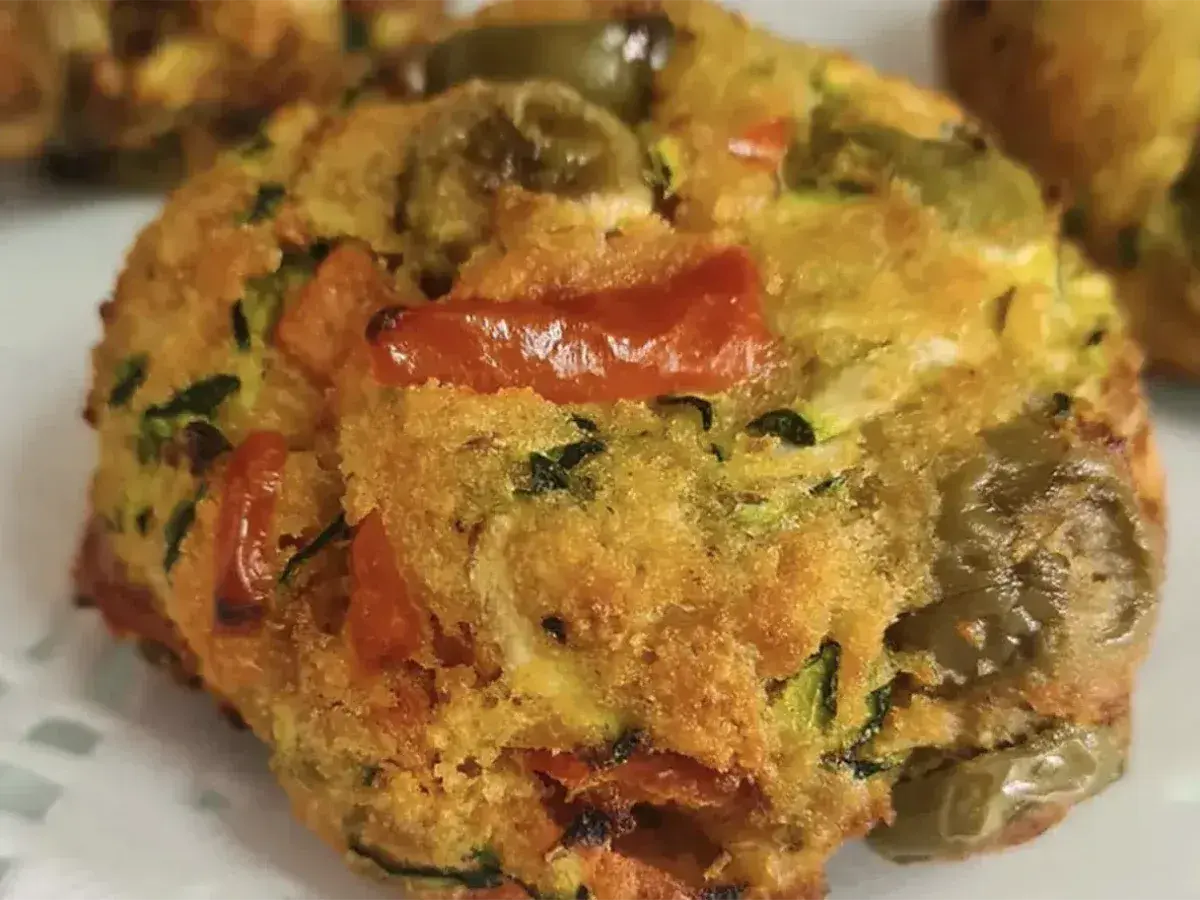 Polpette di zucchine dorate e saporite, con pomodorini e olive verdi, pronte per essere gustate.