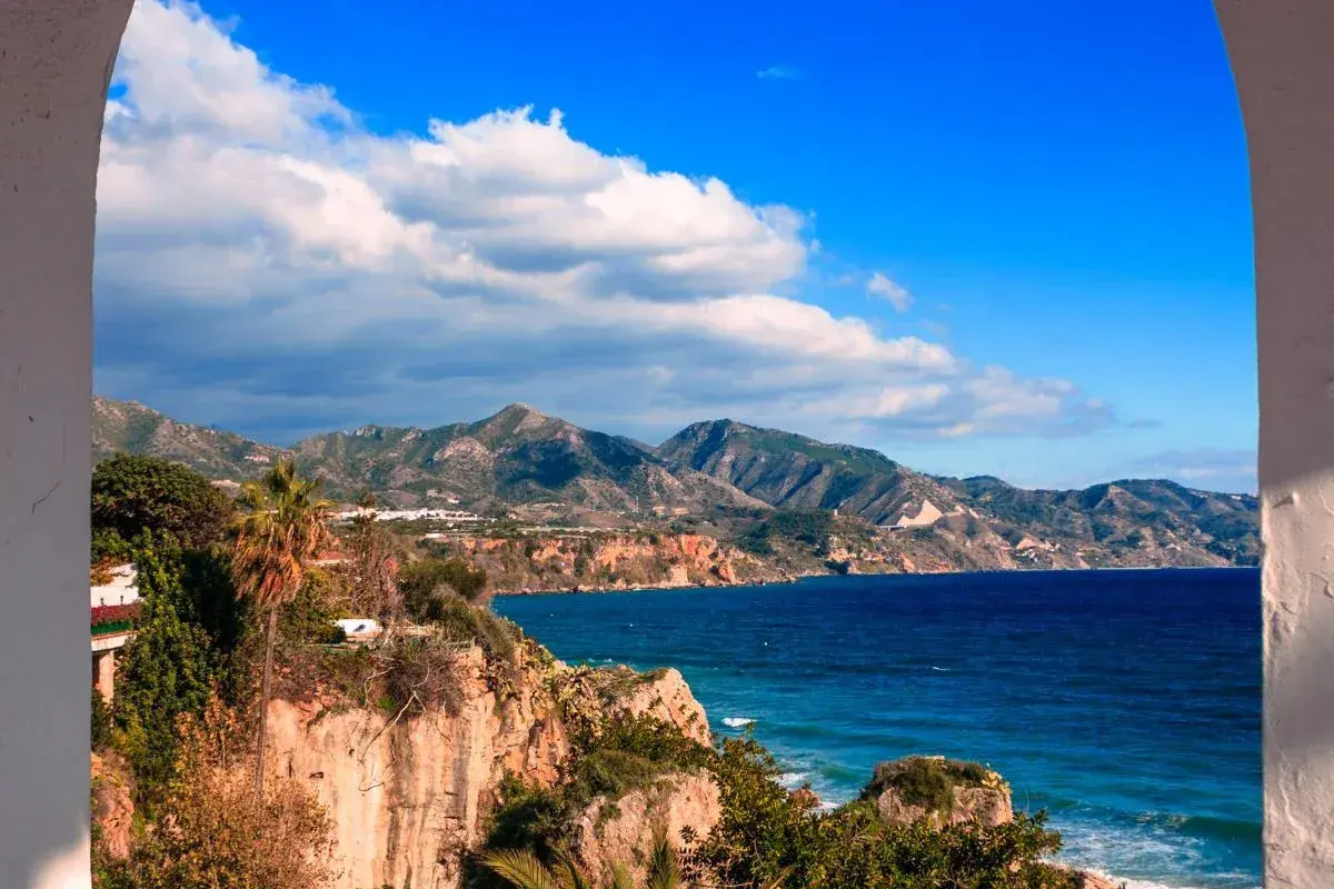 Vue panoramique de la côte andalouse, parfaite pour un guide Malaga. Falaises rocheuses, mer bleue et montagnes verdoyantes sous un ciel d'azur.