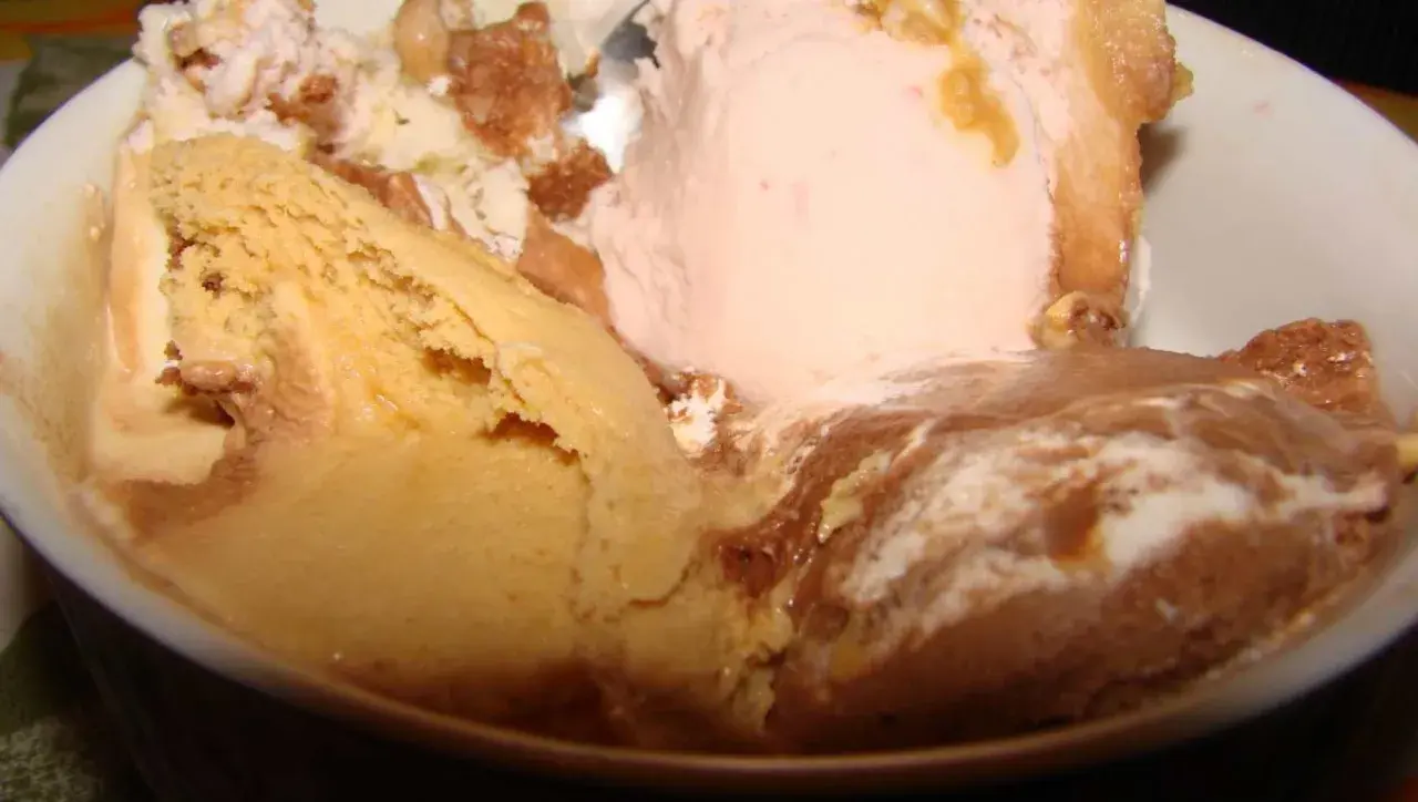 Un tazón lleno de helado de leche cremoso, con sabores de caramelo, fresa y chocolate, adornado con trozos de galleta.
