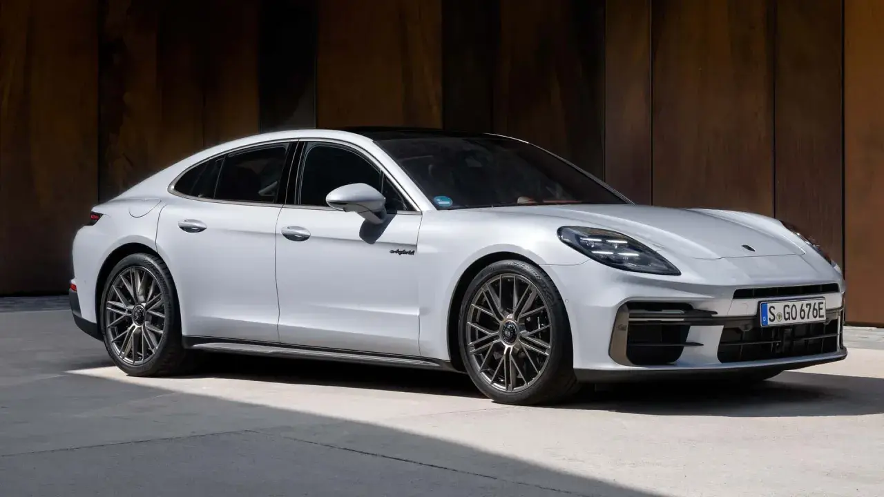 Elegancki, biały Porsche Panamera 2024 z czarnym dachem i przyciemnianymi szybami, zaparkowany na tle rustykalnej ściany.
