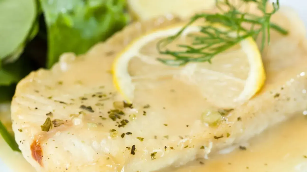Filete de pescado bañado en una deliciosa salsa de limón para pescado, adornado con una rodaja de limón y eneldo.