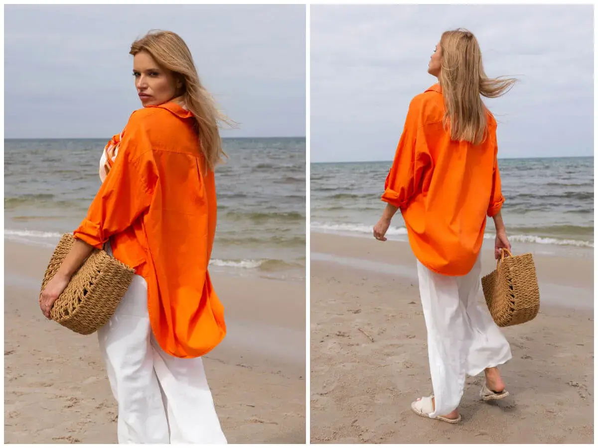 Kobieta w pomarańczowej koszuli i białych spodniach na plaży. Idealne outfity na lato, z plecioną torbą.