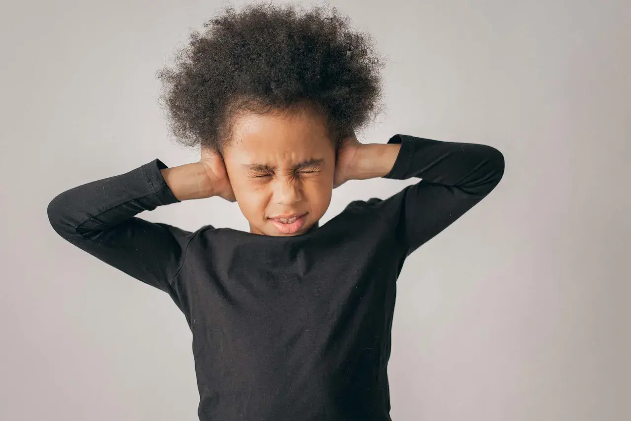 Niño con afro cubriéndose los oídos, mostrando malestar. Sugiere la necesidad de tratamiento para la ansiedad en niños de 5 a 12 años.