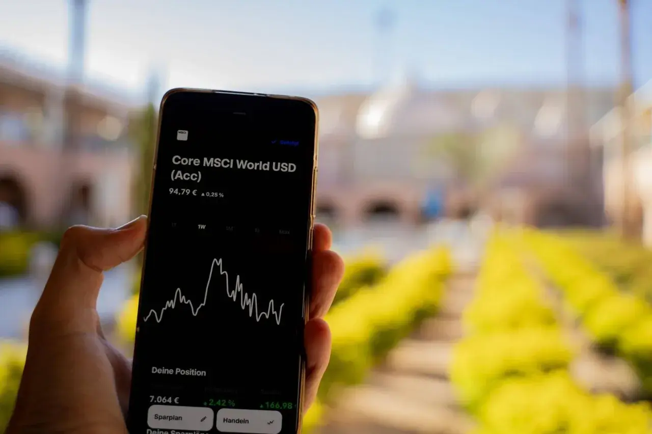 Hand hält Smartphone mit MSCI World Rendite-Chart. Der Kurs steht bei 94,79 € mit einem Plus von 0,25%.