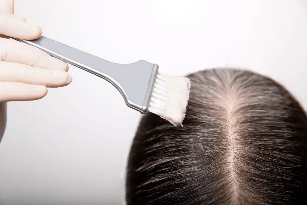 Guanto e pennello applicano tinta sui capelli scuri, mostrando come fare la tinta in casa per un cambio look.