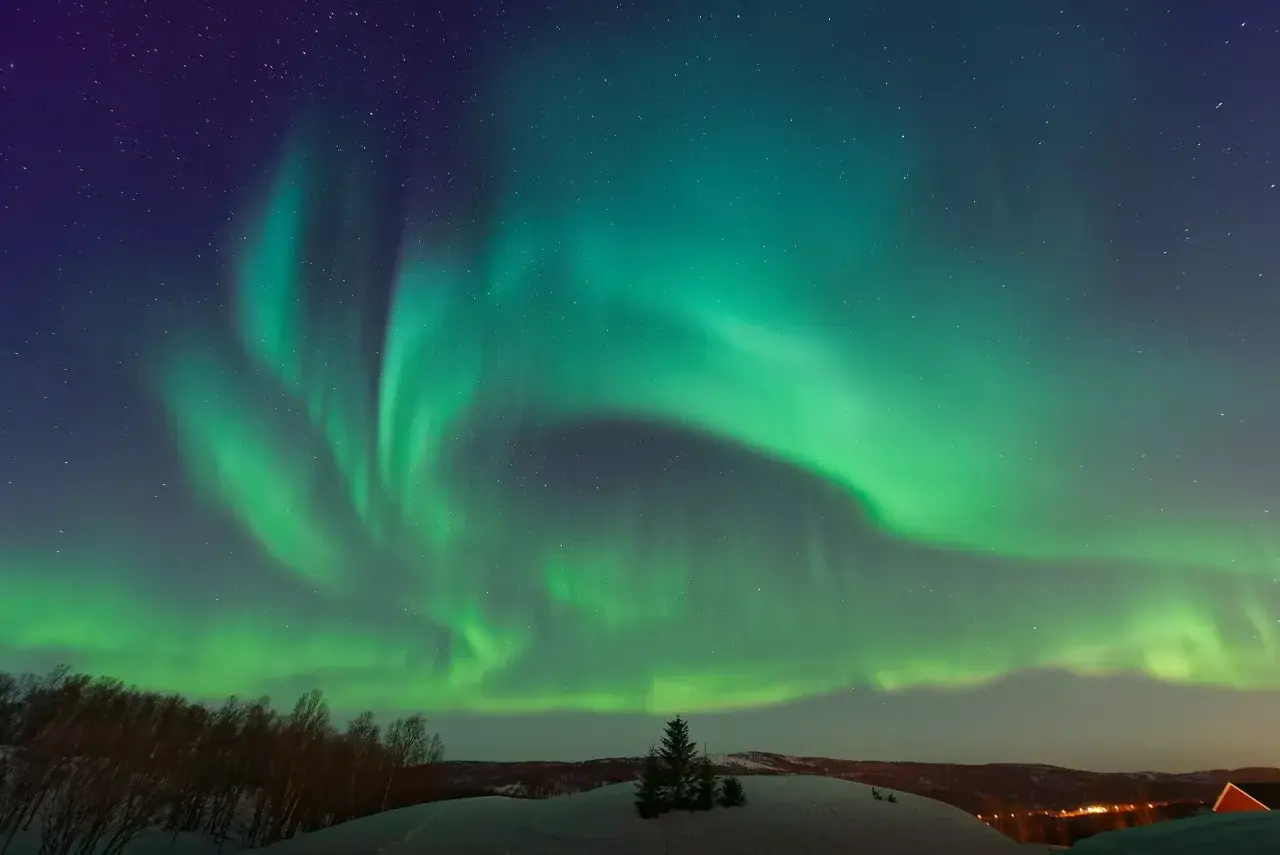 Zielona zorza polarna nad śnieżnym krajobrazem w Norwegii. Niebo rozświetlone tańczącymi światłami.