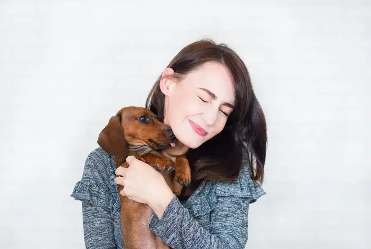 Un perro salchicha le lame la cara a su dueña, que sonríe con los ojos cerrados. Es la prueba de que mi perro me sigue a todas partes.