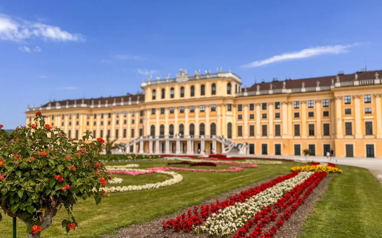 Wiedeń atrakcje: Pałac Schönbrunn z barwnymi rabatami kwiatowymi i zielonymi trawnikami.